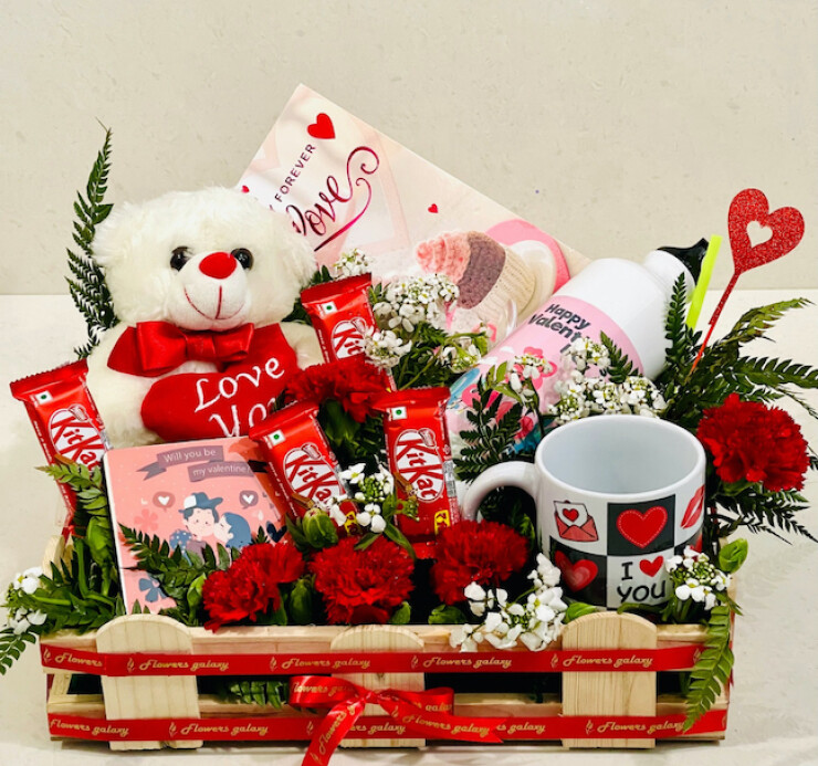 Valentine gift basket with red white teddy, carnations, KitKat chocolates, love mug, bottle and greeting card arranged in pine wood crate