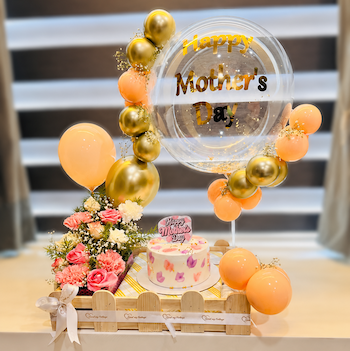 Mother’s Day celebration basket with pineapple cake, fresh flowers, golden peach balloons, and premium bobo balloon arrangement.